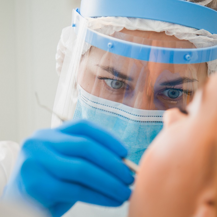 : Dentista con visiera e mascherina che visita paziente